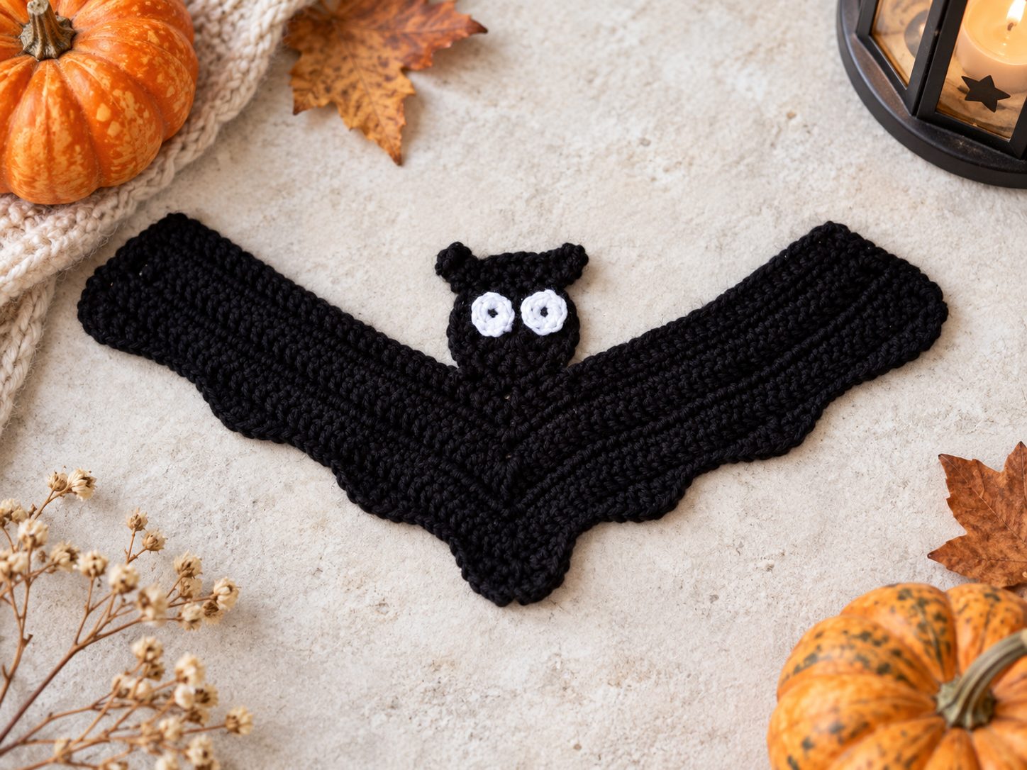 Black crochet Halloween bat applique styled with pumpkins and autumn decor