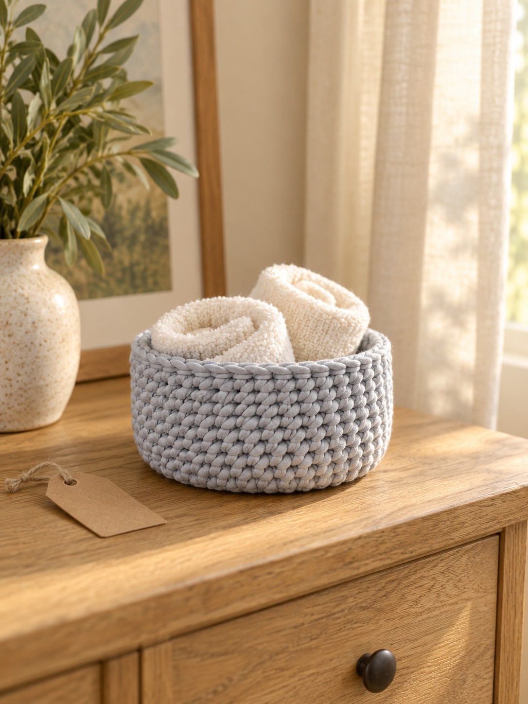 AI-styled illustration of a low gray crochet basket holding rolled ivory cloths